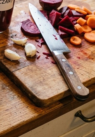 Pokrojone świeże buraki, czosnek i nóż kuchenny na desce do krojenia